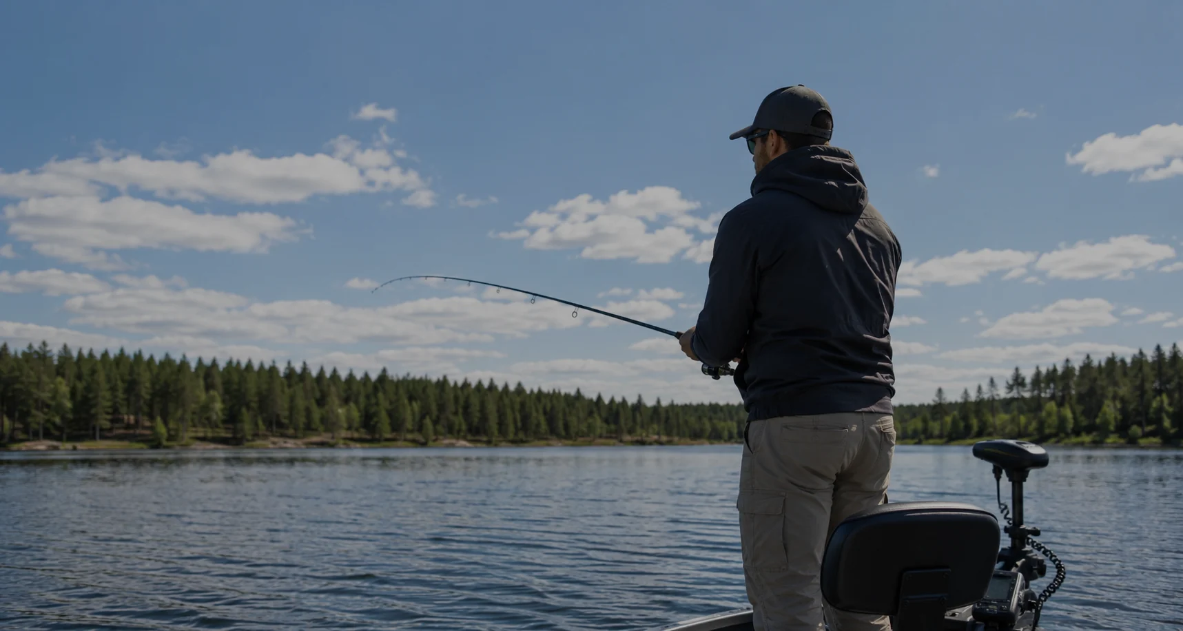 Sportfiskare som kastar med spinnspö från en båt på en skogsomgiven sjö